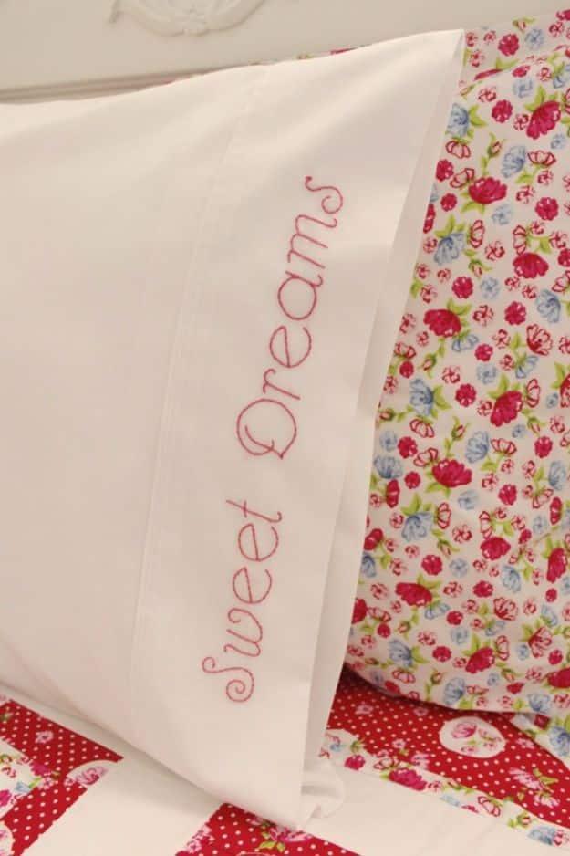 White pillowcase cuff hand embroidered with pink backstitched script reading Sweet Dreams, beside floral bedding