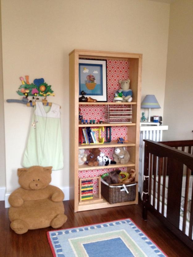 Nursery bookcase backed with red and white patterned wrapping paper and filled with books, toys and art
