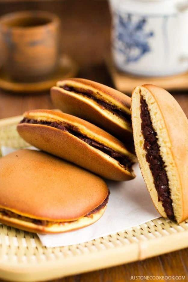 Japanese red bean pancakes, dorayaki, standing on edge on a woven bamboo mat with the front one cut open to show the filling