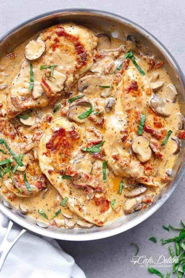 Creamy sun dried tomato parmesan chicken in a skillet with mushrooms, red tomato strips and fresh basil