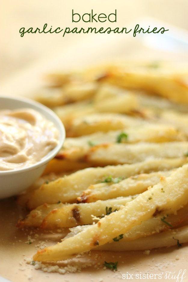 Baked garlic parmesan fries on a foil lined sheet pan with parsley and a bowl of spicy aioli for an outdoor barbecue