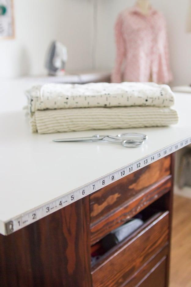 Cutting table with measuring tape, a measuring tape glued along the front edge of a white cutting table beside folded fabric