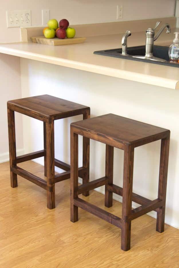 Two half lap bar stools built from 2x4s with dark stained square legs, sitting at a kitchen counter on a wood floor