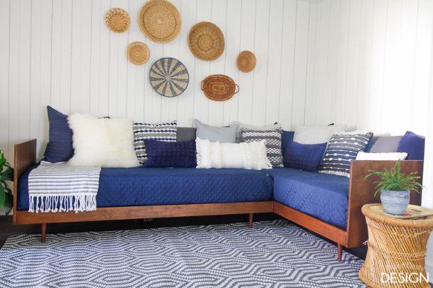 Walnut stained plywood daybed with tapered legs and one raised armrest, navy quilted cover and woven wall baskets