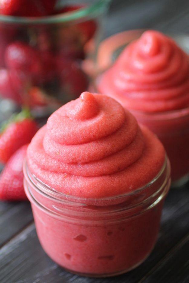 Strawberry dole whip swirled into two small glass jars, deep pink soft serve with fresh berries behind
