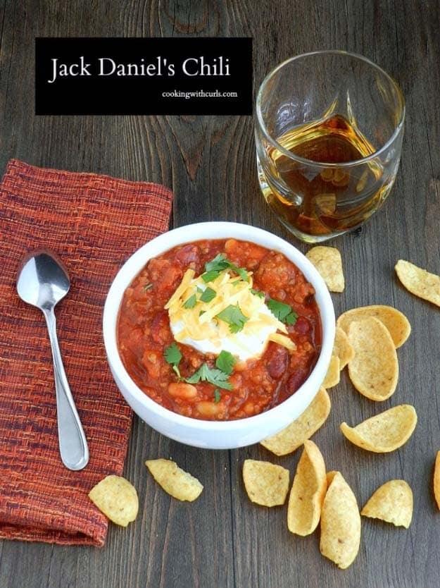 Jack Daniels chili in a white bowl topped with sour cream, grated cheese and cilantro with corn chips