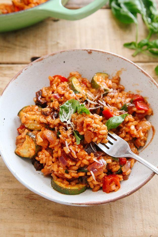 Bowl of tomato risotto with roasted courgette and red pepper, topped with basil and vegan parmesan, and a fork