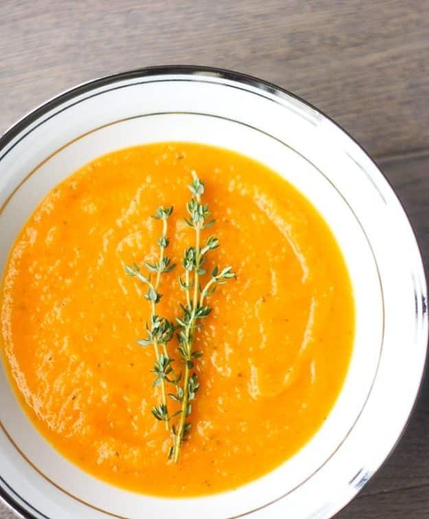 Roasted butternut squash soup in a white bowl with a gold rim, deep orange with a thyme sprig on top