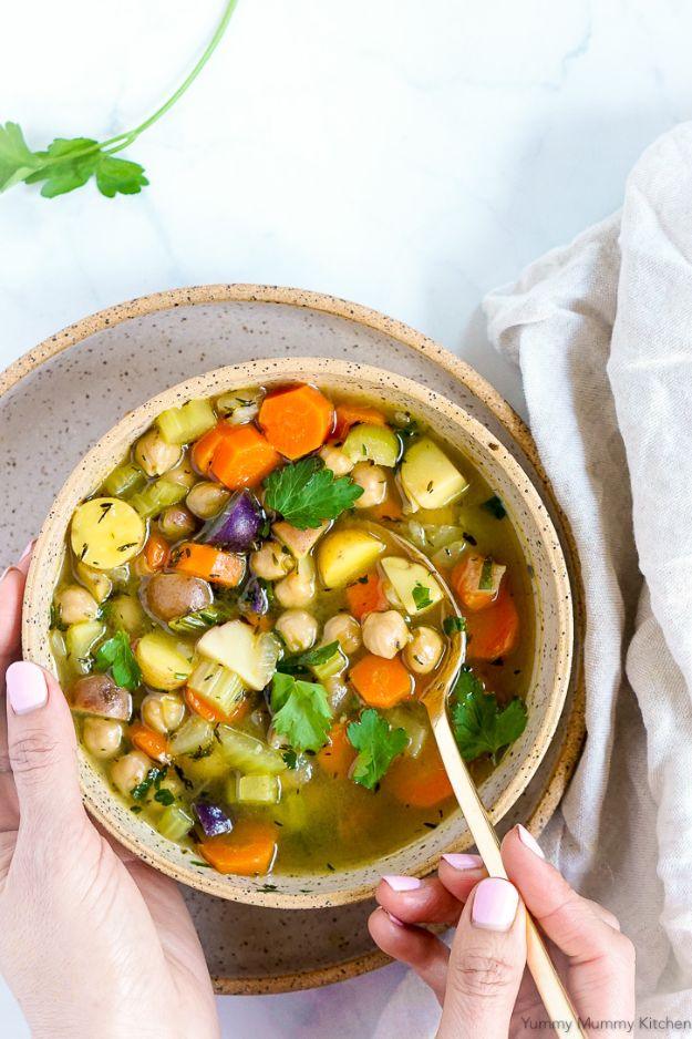 Chickpea vegetable soup in a speckled bowl held in two hands, full of chickpeas, carrots, celery and potato