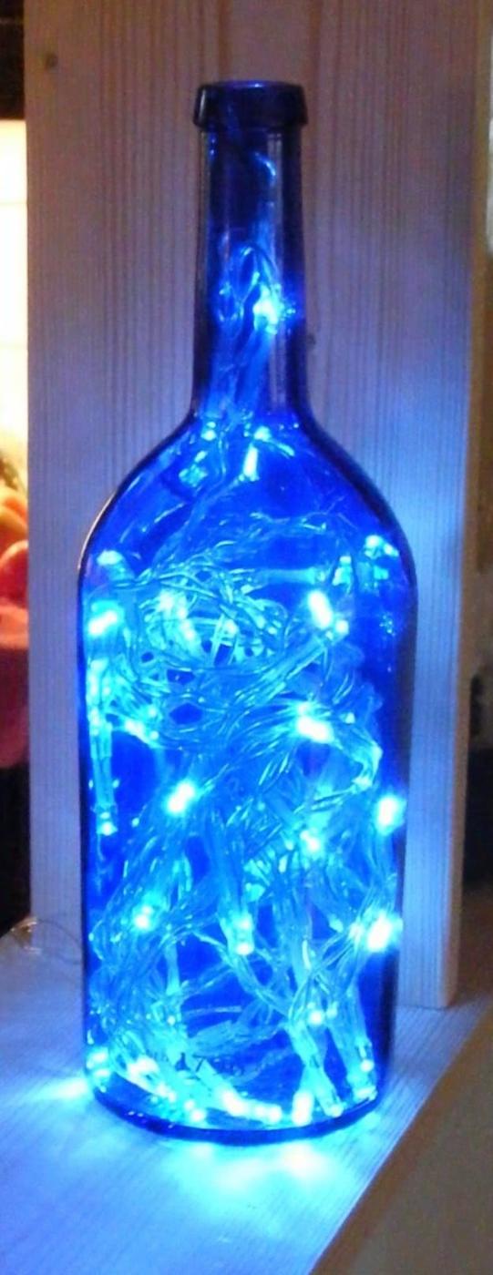 String light wine bottle lamp, a blue bottle filled with glowing white fairy lights against a wood wall