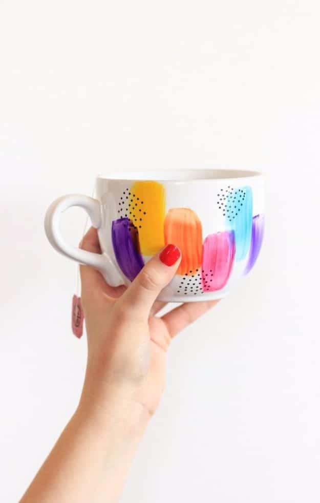 Dishwasher safe decorated mugs, a hand holding a white mug painted with bright brushstrokes and black dots