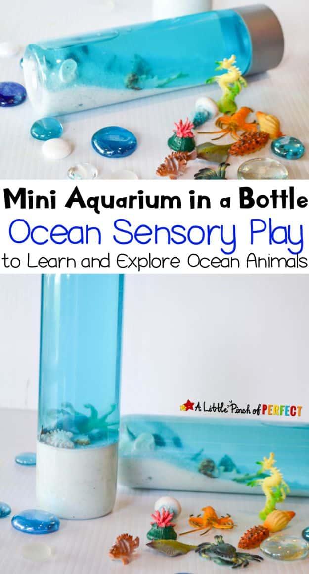 DIY aquarium sensory bottle with blue water, white sand and small plastic sea creatures beside glass pebbles