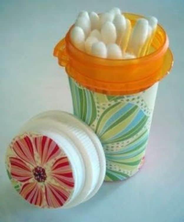 Pill bottle covered in green patterned paper and filled with cotton swabs, beside a second decorated bottle lid