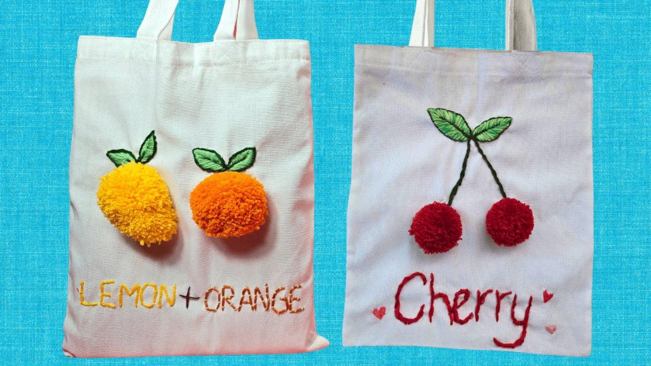 Fruit embroidered tote bags, two canvas totes with embroidered stems and leaves and yellow, orange and red pom poms as fruit