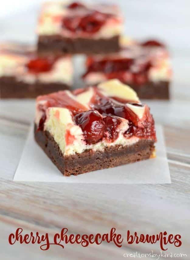 Cherry cheesecake brownies cut into squares with a cocoa base, cream cheese layer and red cherry topping