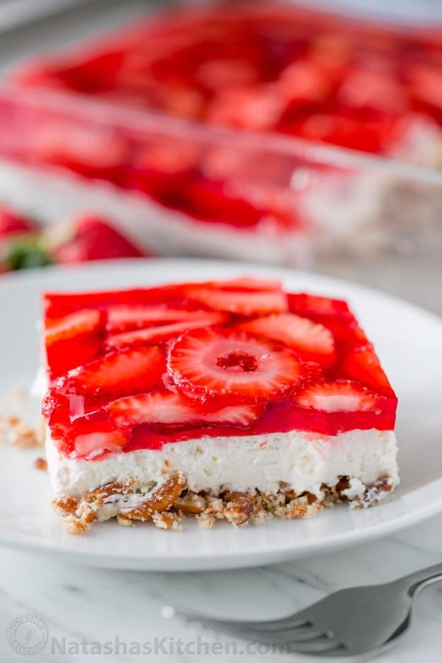 Strawberry pretzel salad in a glass dish with a red jello layer and cream cheese filling, a potluck dessert idea