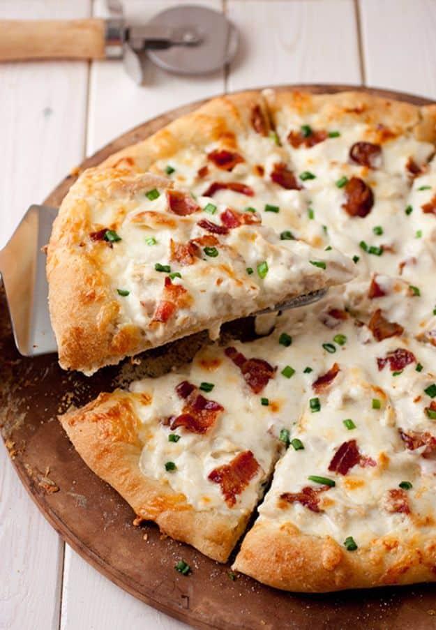 White chicken alfredo pizza with melted cheese, bacon and chives, one slice cut, on a round wooden board