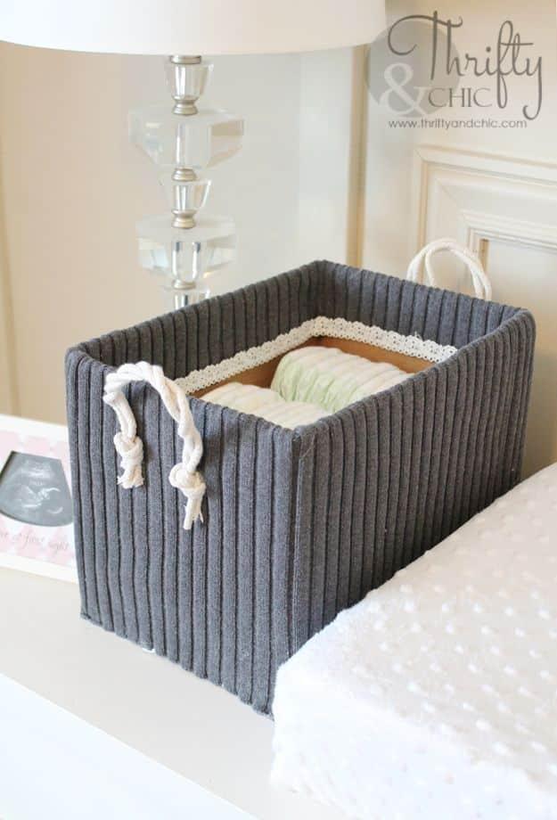 Cardboard craft storage box covered in a grey ribbed sweater with white rope handles sitting on a bed