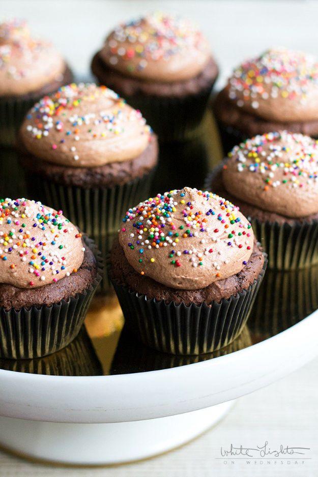 Easy chocolate pudding cupcakes with swirled chocolate frosting and rainbow sprinkles on a white cake stand
