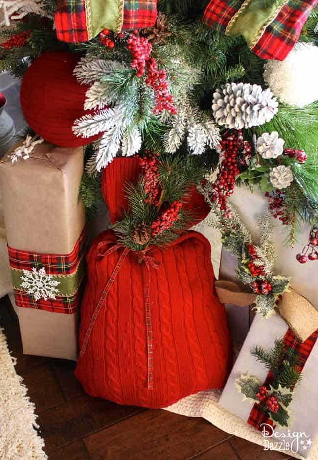 A red cable knit sweater turned into a gift sack, tied with ribbon and a pine sprig under a Christmas tree