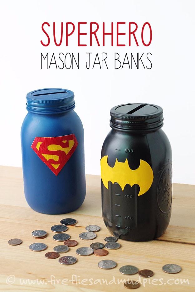 Mason jar superhero banks, a blue Superman jar and a black Batman jar with coin slot lids and scattered coins