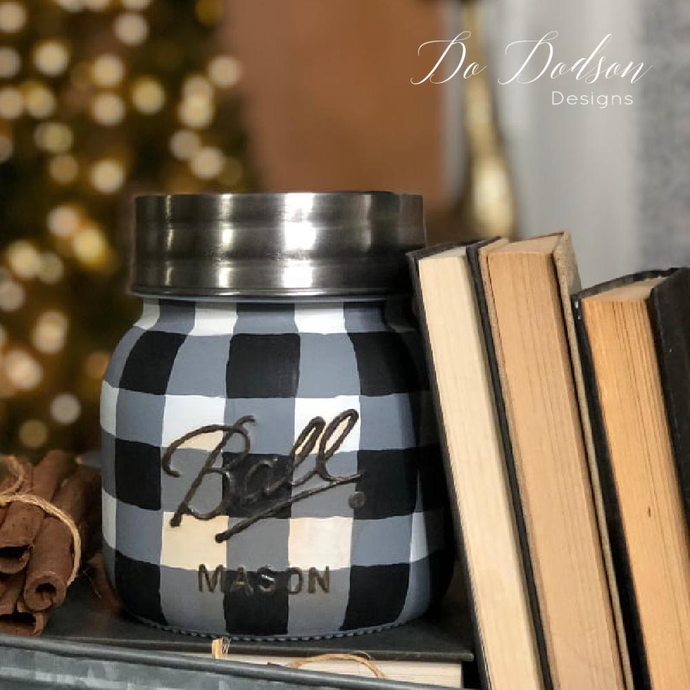 Wide mouth glass canister hand painted in black and white buffalo plaid, standing on a rustic wooden shelf