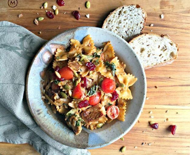 Chicken kale pasta in a pale blue bowl with dried cranberries, pumpkin seeds and cherry tomatoes on top