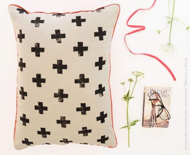 White cushion printed with a scattered black cross pattern and red piping on a pale floral background