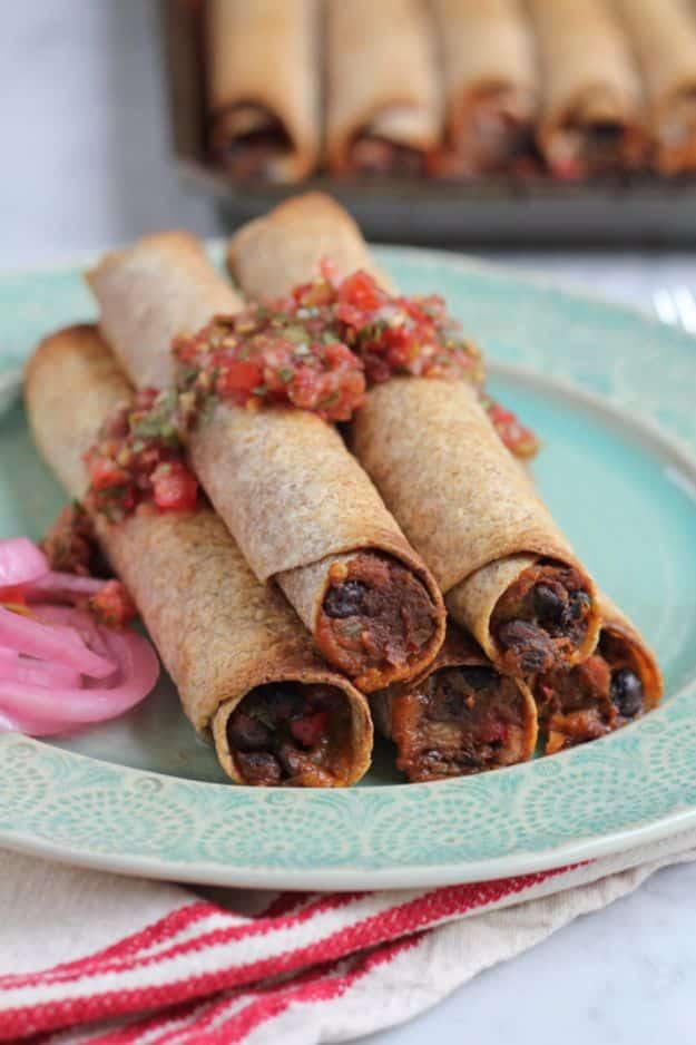 Baked veggie taquitos rolled tight and topped with red salsa on a mint green plate with pickled red onions