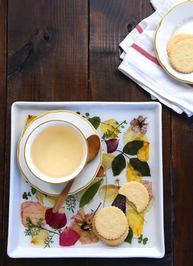 DIY pressed rose petal tray, a white square tray of pressed petals and leaves under epoxy holding a teacup and shortbread