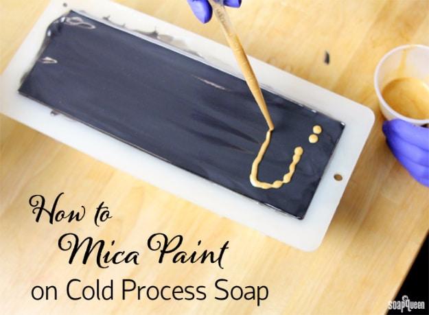 Mica paint on cold process soap, gold mica lines being dropped onto a wet black soap loaf in a white silicone mold