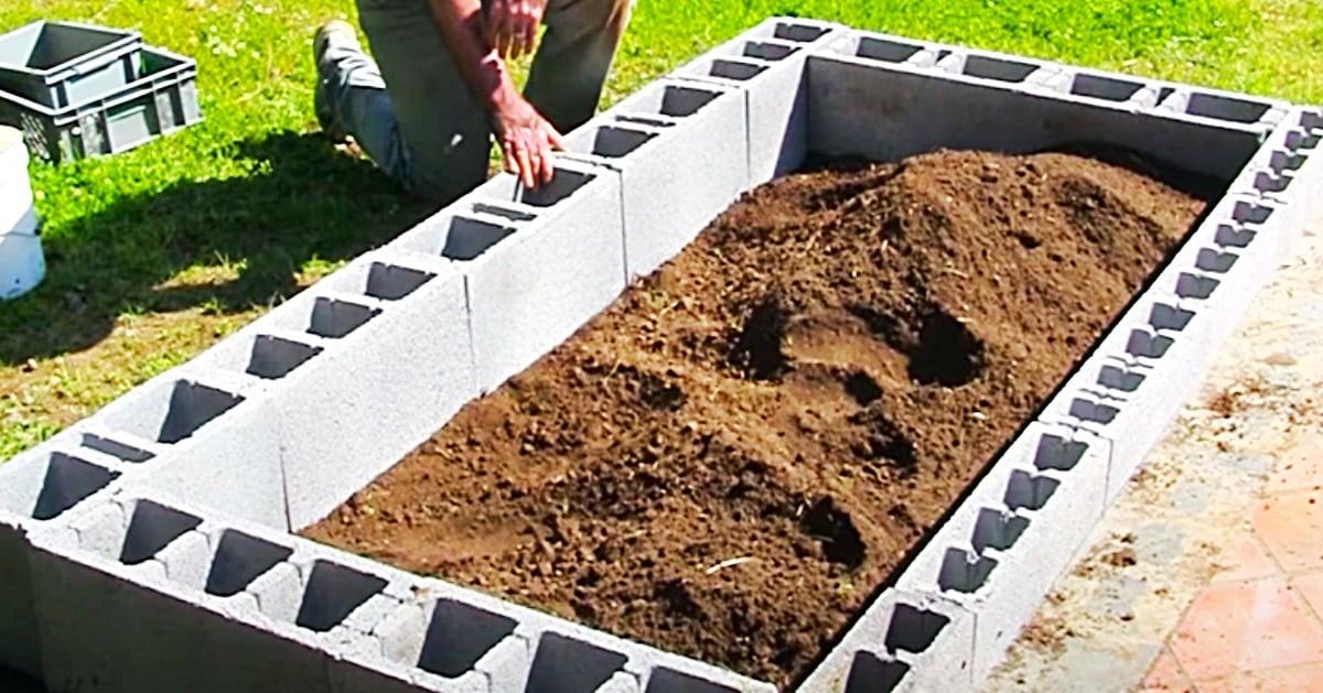 Newly built cinder block raised bed filled with dark soil on a lawn, with a person kneeling at one corner