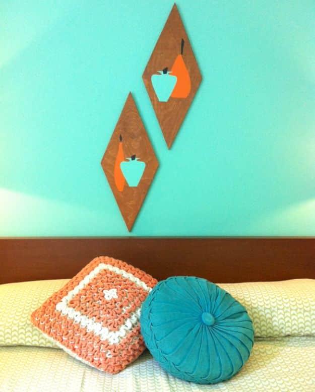 Two stained plywood diamond wall plaques with orange and turquoise stencilled apples on a bright teal bedroom wall