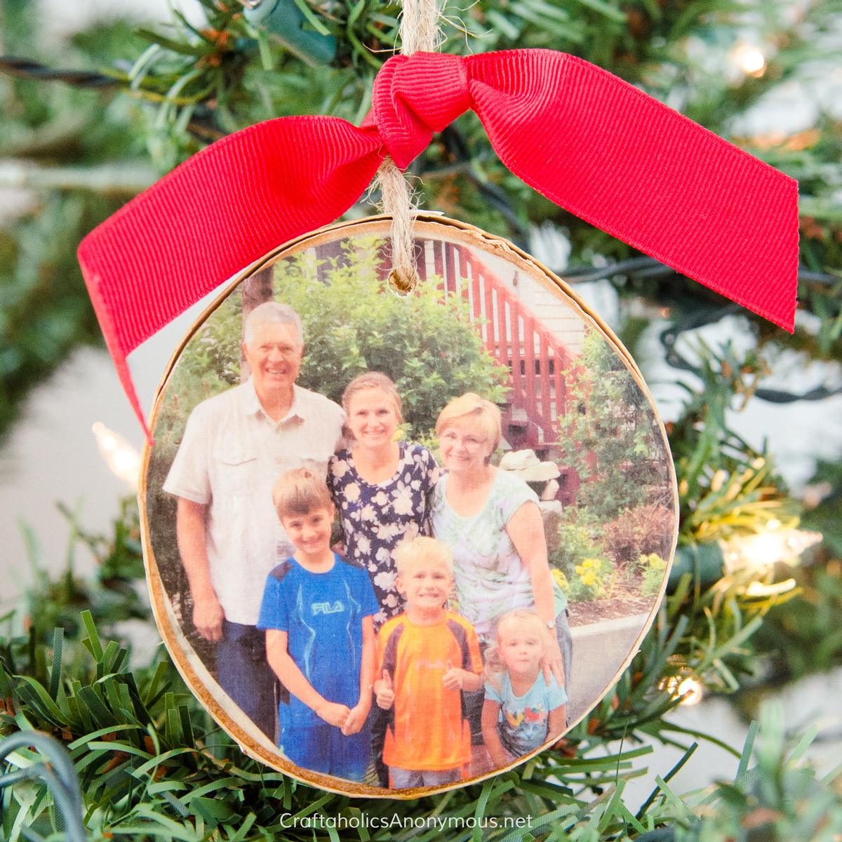 Round wood slice ornament with a family photo transferred onto the wood, hung by red ribbon and twine on a tree