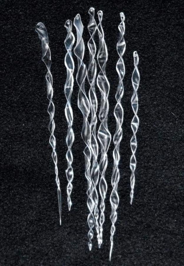 Seven clear twisted icicle ornaments cut and heat shaped from plastic bottles, laid out on black velvet fabric
