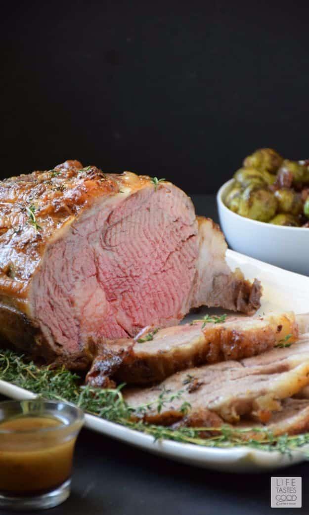 Garlic crusted prime rib roast carved on a white platter, rosy pink center with thyme and a gravy boat