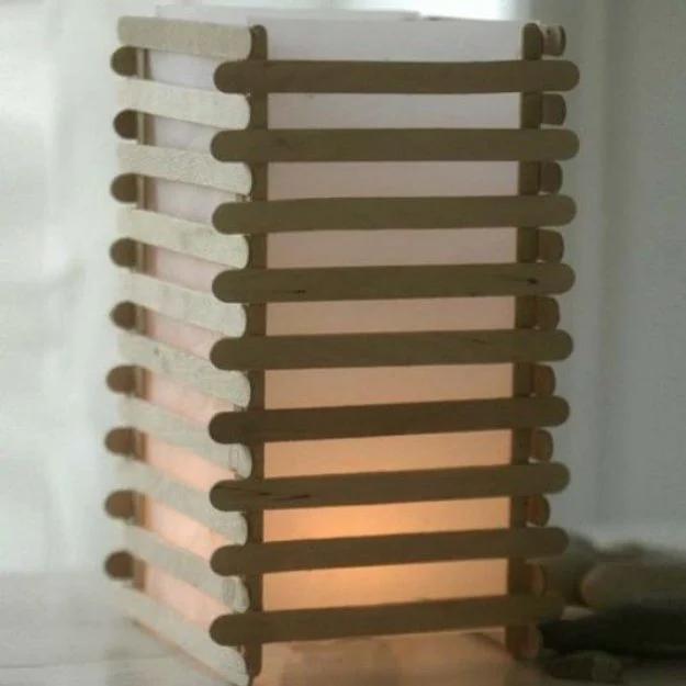 Square lantern built from horizontal wooden lolly sticks glowing from a candle behind translucent paper inside
