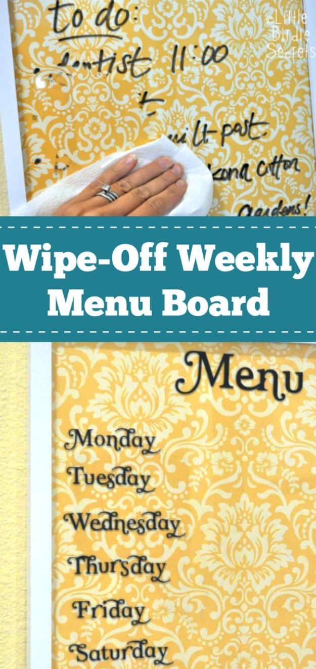A framed weekly menu board with wipe off lettering hangs in a kitchen, a marker resting on the shelf beneath it