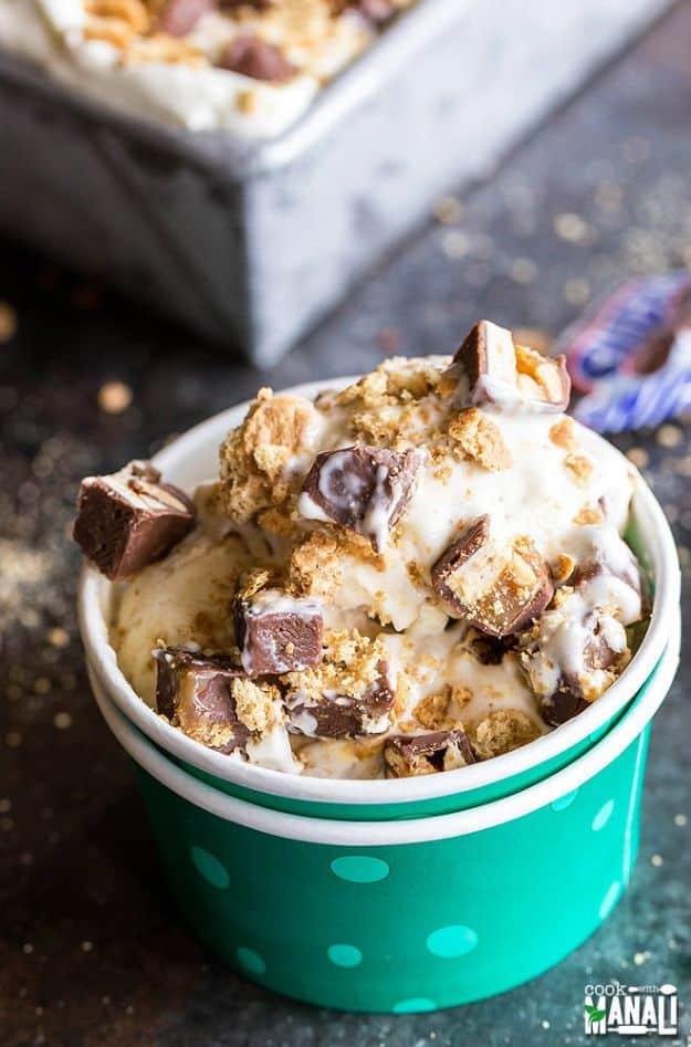 No churn Snickers cheesecake ice cream in a loaf pan with chopped candy bars and graham cracker pieces