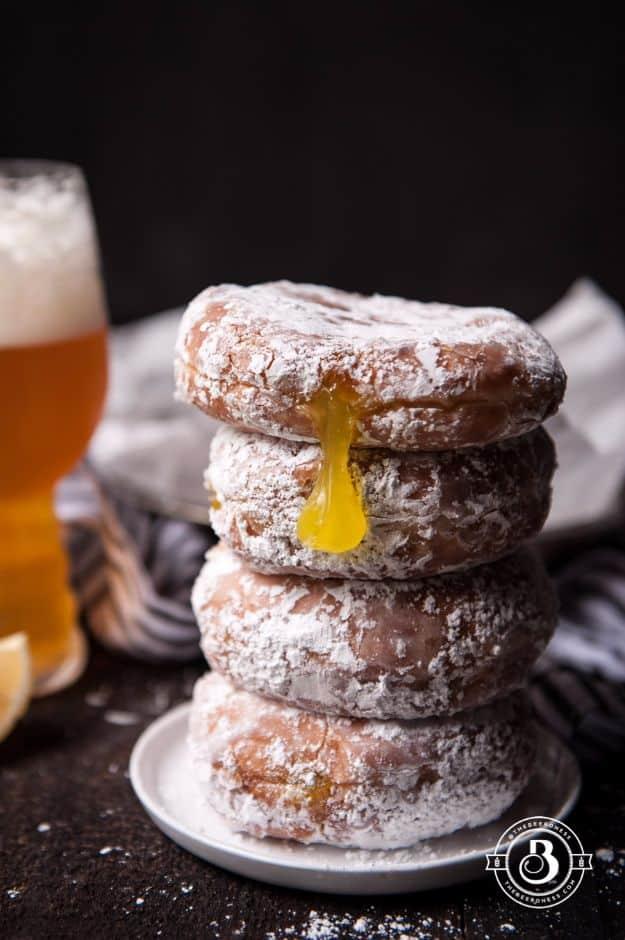 Beer doughnuts stacked on a plate and dusted with sugar, lemon curd dripping down, a beer glass behind