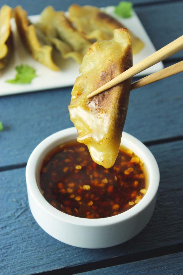 Pleated gluten free potsticker held in chopsticks over a bowl of chili dipping sauce, more on a plate