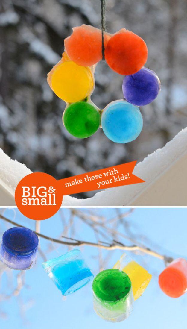 Rainbow ring of frozen colored ice discs hanging from a snowy branch, with small colored ice cups hung below