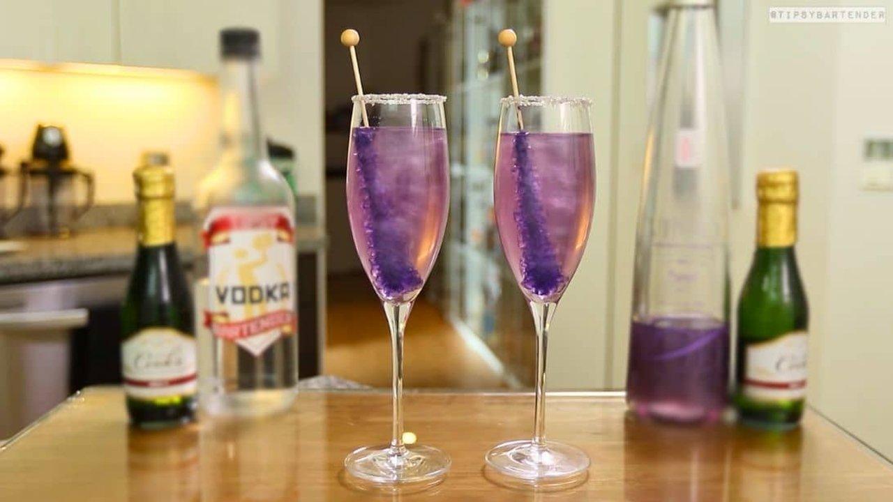Two silver sugar rimmed flutes of pale lavender shimmering champagne, each with a purple rock candy stick