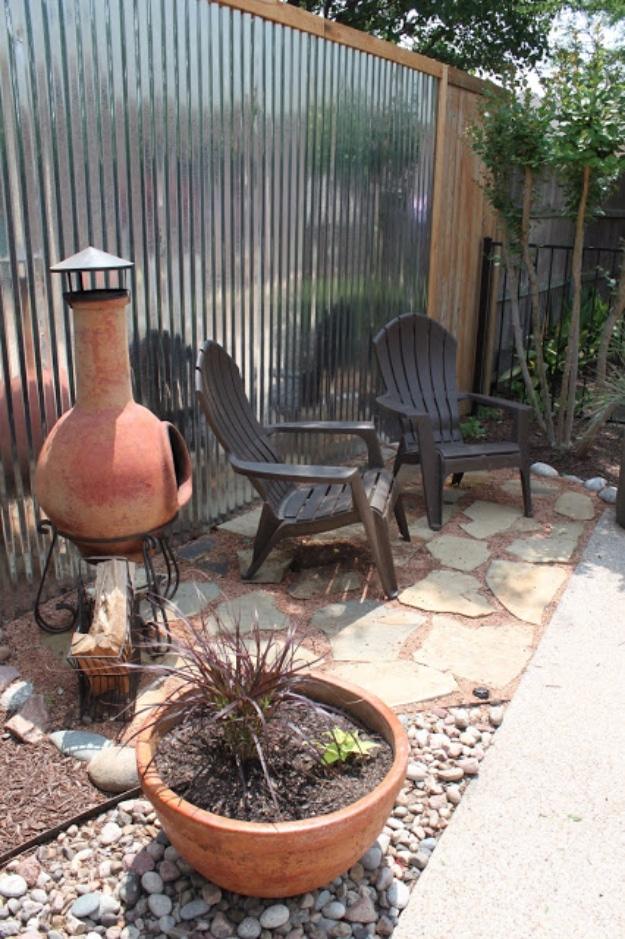 Tin accent wall fence, a corrugated metal wall framed in wood behind two dark patio chairs and a clay chiminea on flagstones