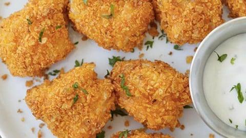 Crunchy Dorito crusted chicken tenders cooked golden orange and scattered on a white plate with a bowl of ranch