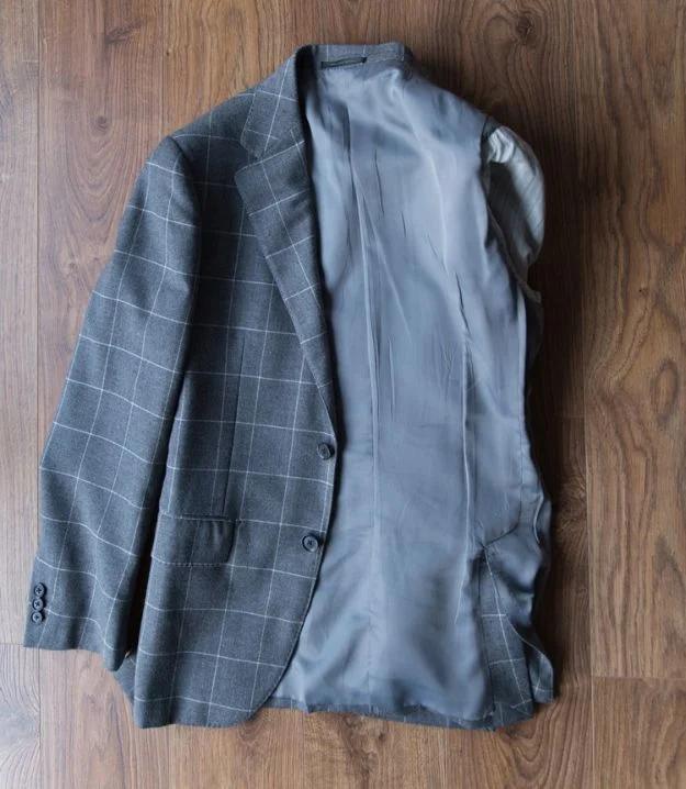 Grey windowpane check blazer laid flat on a wood floor with one side turned inside out showing the lining