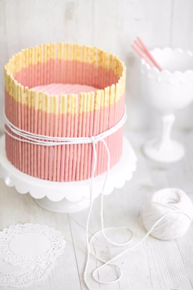 Small pink vanilla birthday cake wrapped in strawberry Pocky sticks and tied with white string on a plate