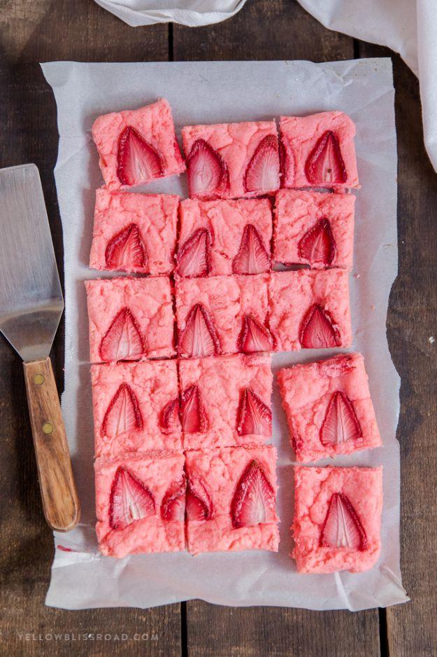 Strawberry brownies cut into twenty pink squares on parchment, each with a sliced strawberry baked into the top