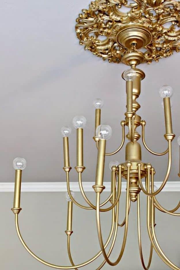 Brass painted chandelier with bare globe bulbs hanging below an ornate gold ceiling medallion made from an old clock