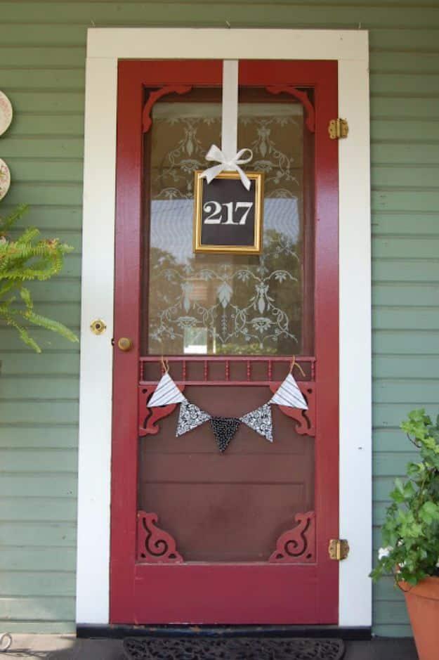 DIY house number frame with black chalkboard numbers hung on wide white ribbon against a red screen door